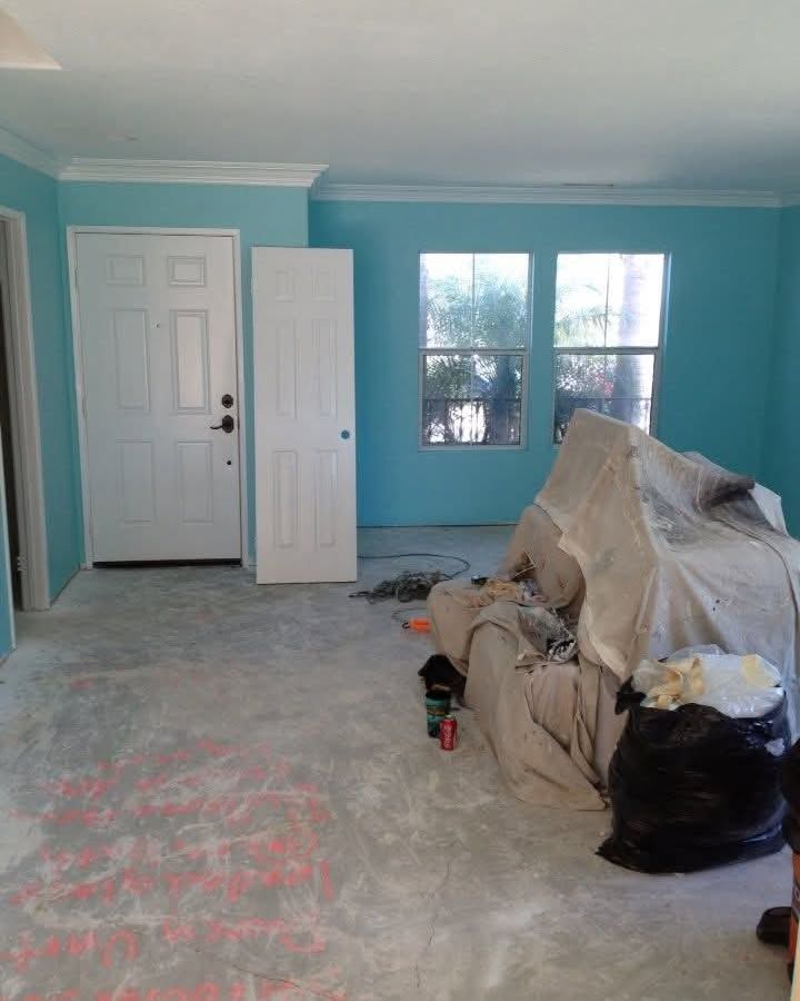 Blue room under renovation with covered furniture, bare concrete floor, and white front door.