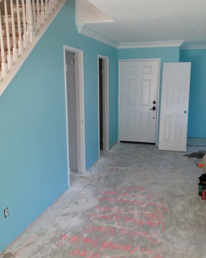 Empty blue hallway with white doors, staircase railing, and unfinished concrete floor.