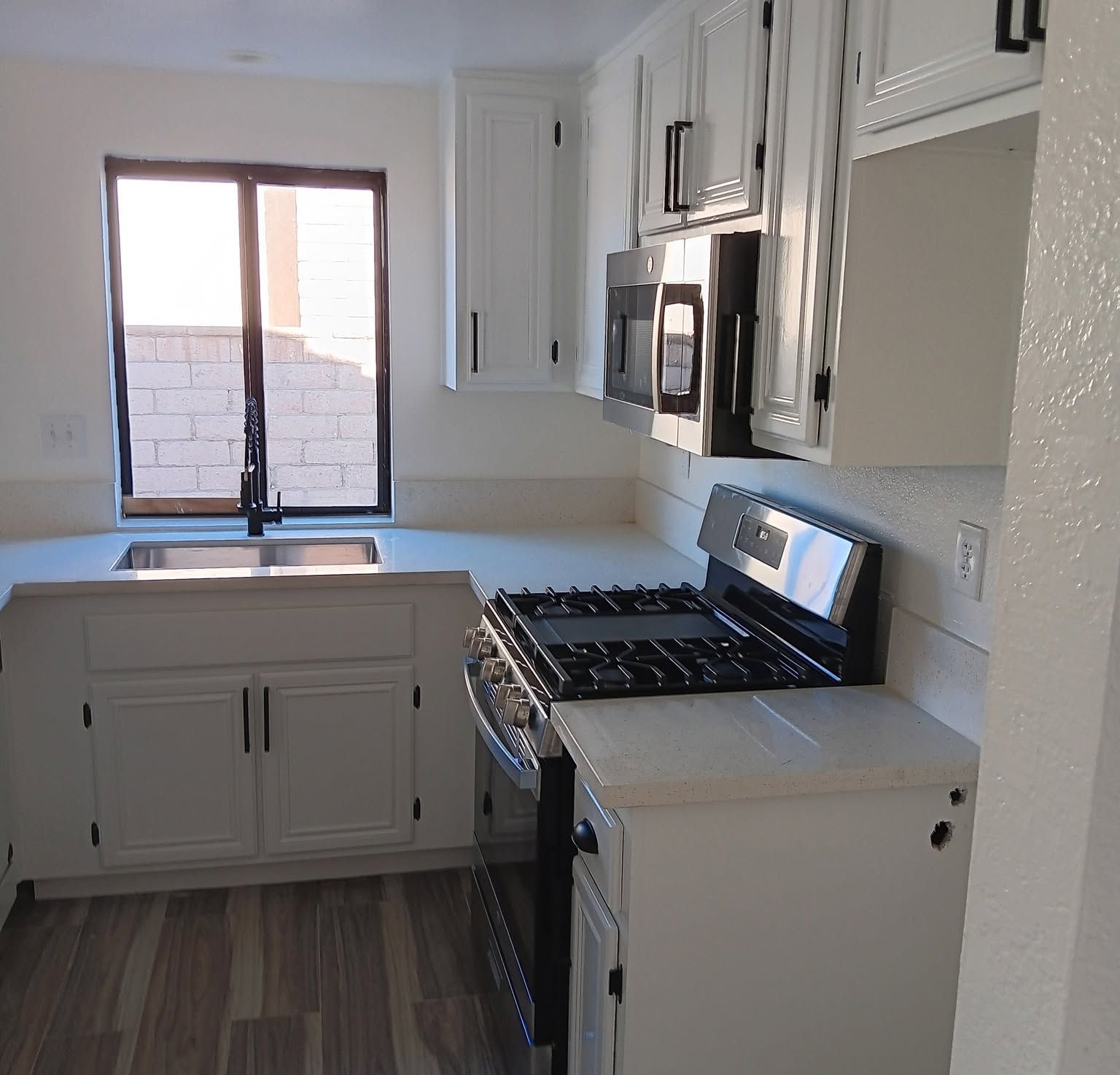 Bright white kitchen with gas stove, sink by window, and built-in microwave cabinets