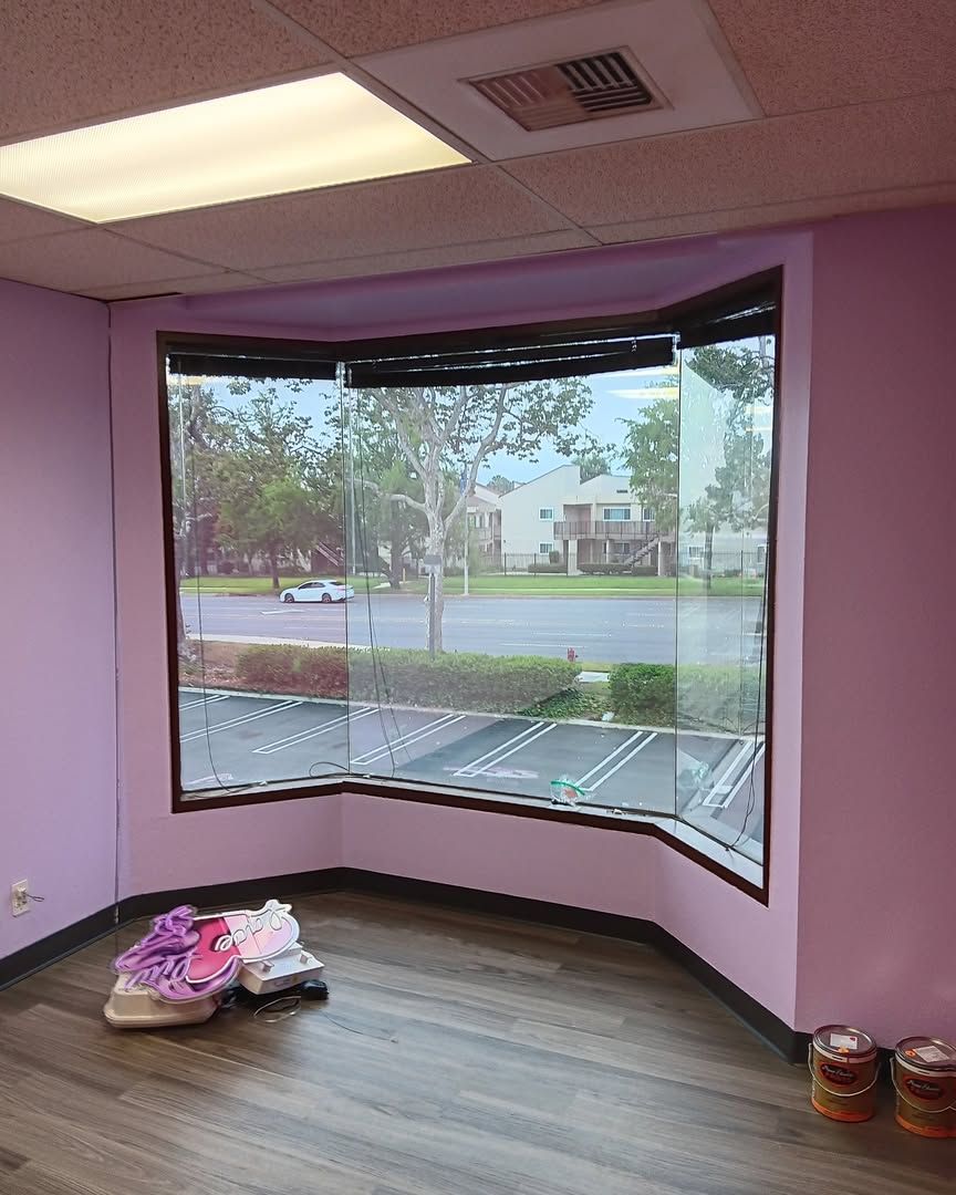 Empty pink room with large bay window, wood-look floor, and shoes on the floor near the wall.