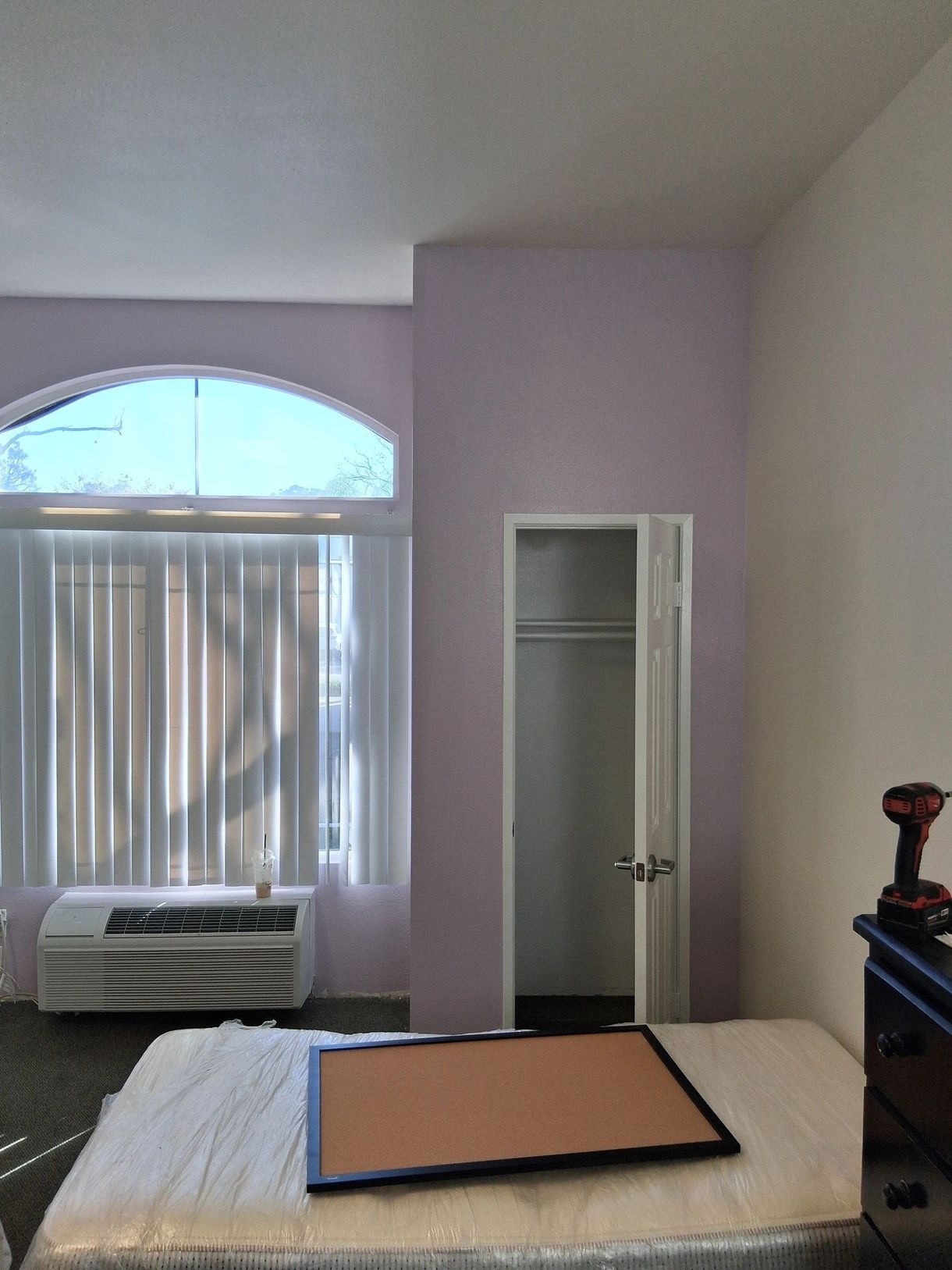 Small bedroom with a bed, window air conditioner, open closet, and a board on the bed.