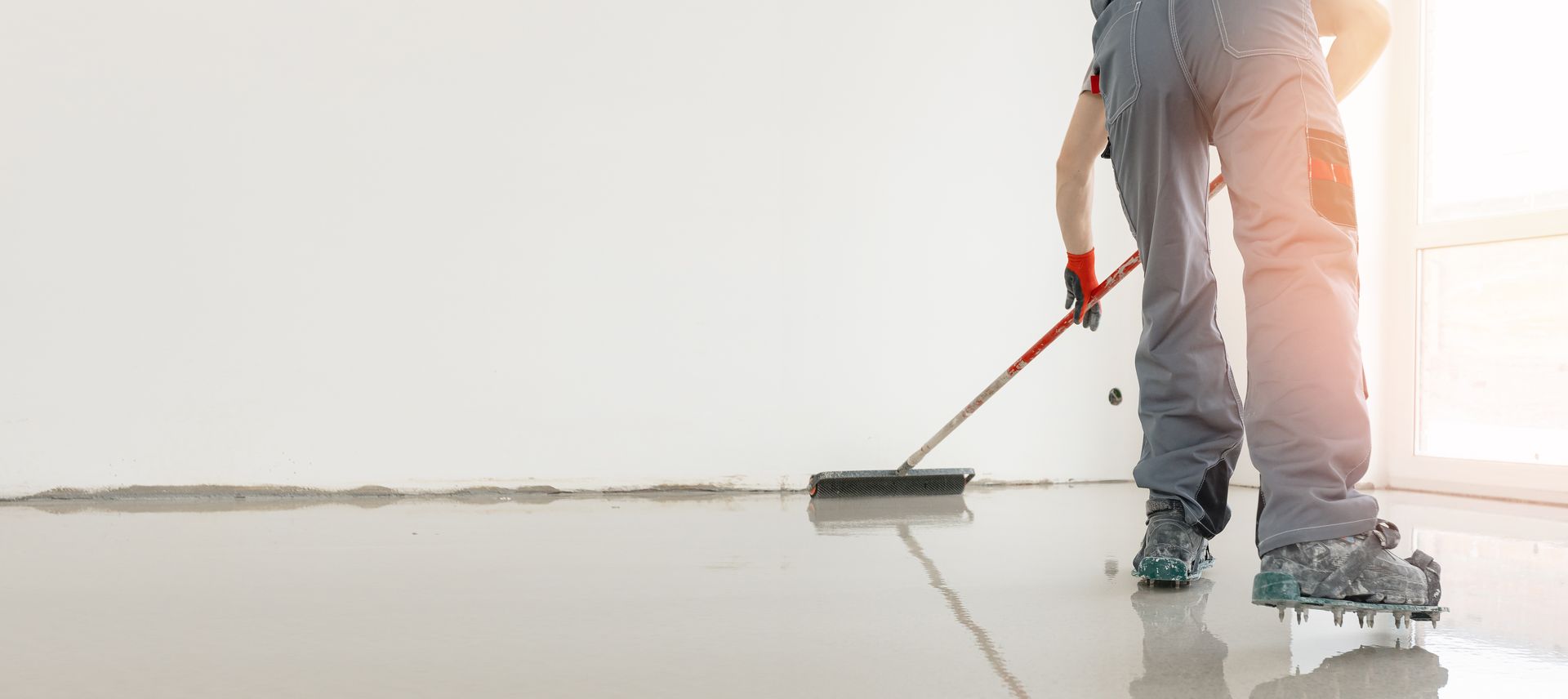 Person painting a white wall with a roller on a floor, bright room, close-up