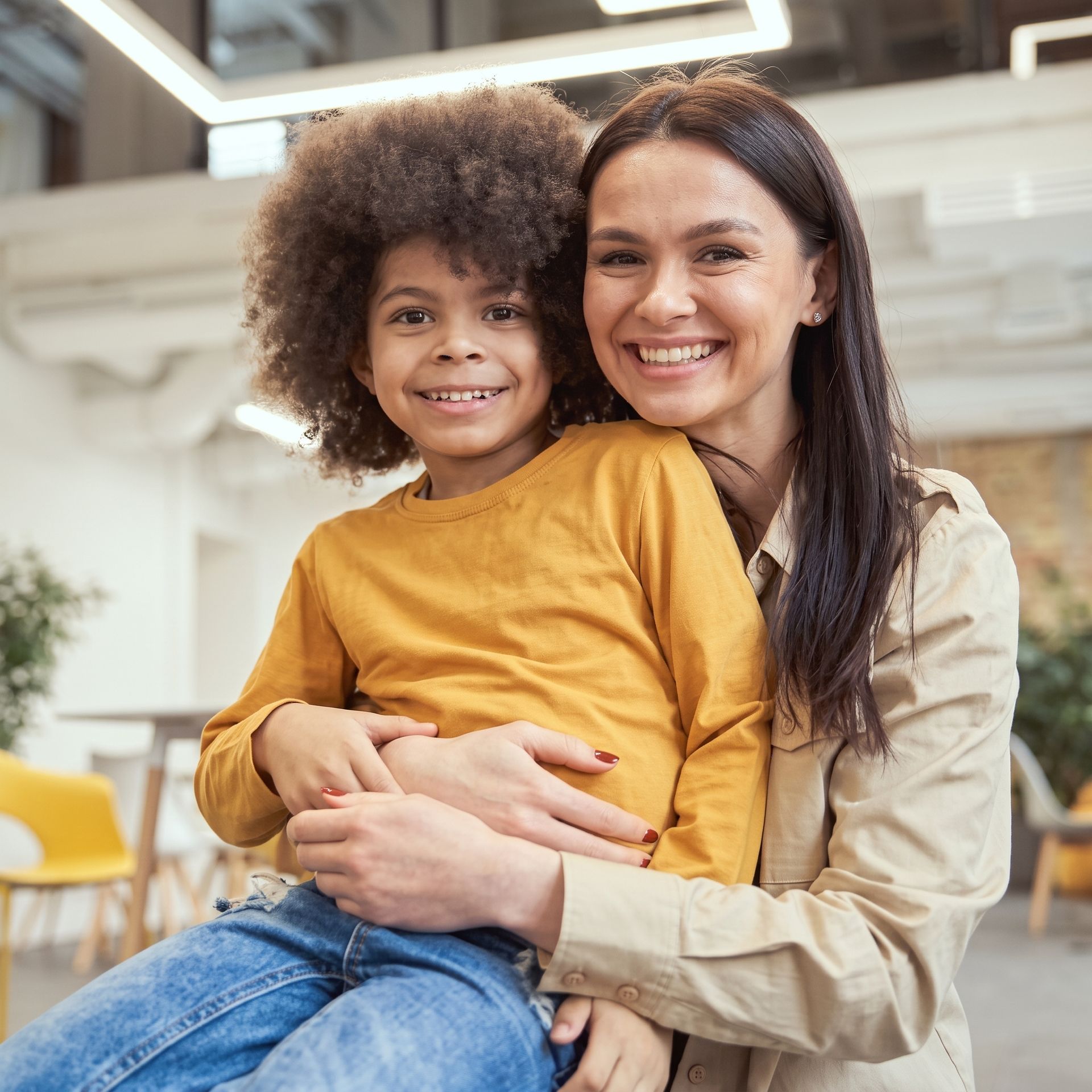Smiling adult holding a child in a bright indoor setting, both wearing casual clothes