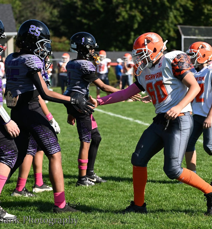 Football players in action on a grassy field; one runs with the ball, pursued by two opponents.