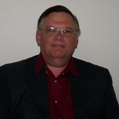 Henry Hudson wearing glasses and a suit is standing in front of a white wall.
