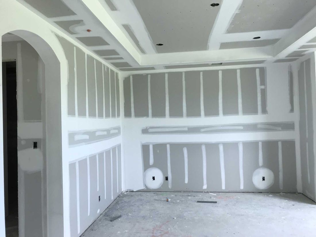 Interior room under construction, featuring drywall on walls and ceiling, with unfinished joints.