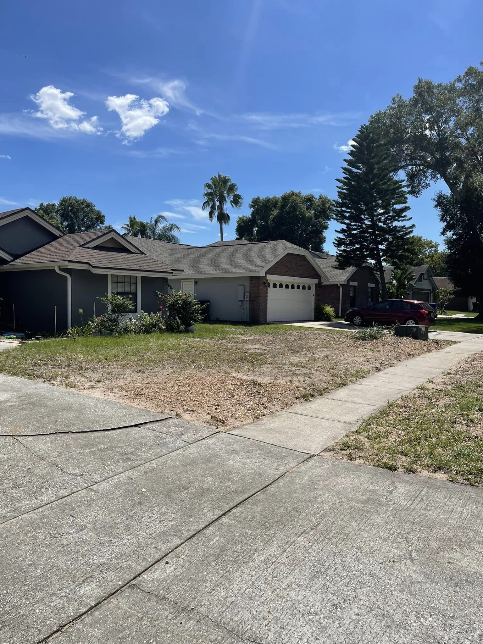 Suburban houses with brown roofs, trees, and a driveway under a blue sky.