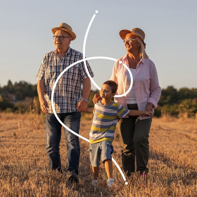 Grandparents and grandchild walk hand-in-hand in a field at sunset.
