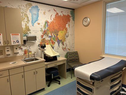 Exam room with world map wall, examination table, sink, and scale.