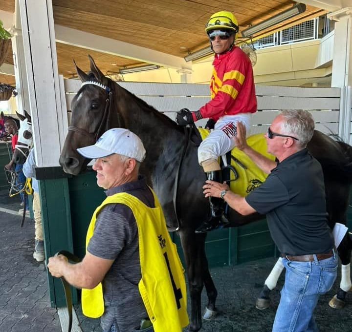 A jockey is riding a horse with two men standing next to it.