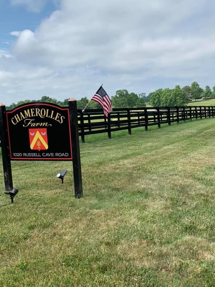 A sign for chamerole 's farm is in the middle of a grassy field.