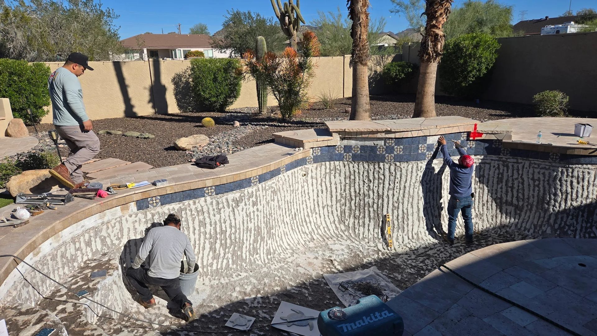 Workers lining and plastering a curved backyard pool under construction in a sunny desert yard