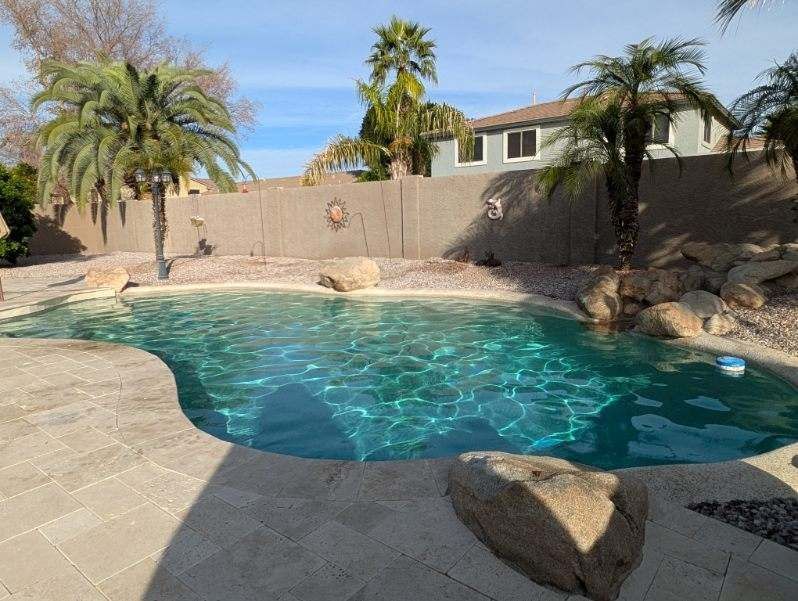 Backyard pool with clear blue water, desert landscaping, palm trees, and a stucco house in the background