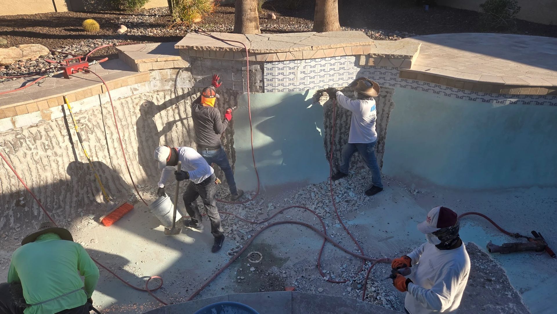 Workers repairing a drained swimming pool, with hoses and tools in a concrete basin.