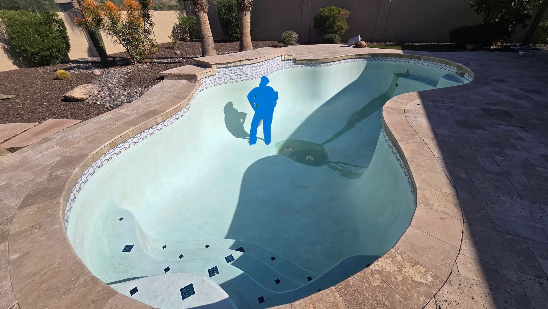 Empty backyard swimming pool with light blue interior and stone deck in desert landscaping