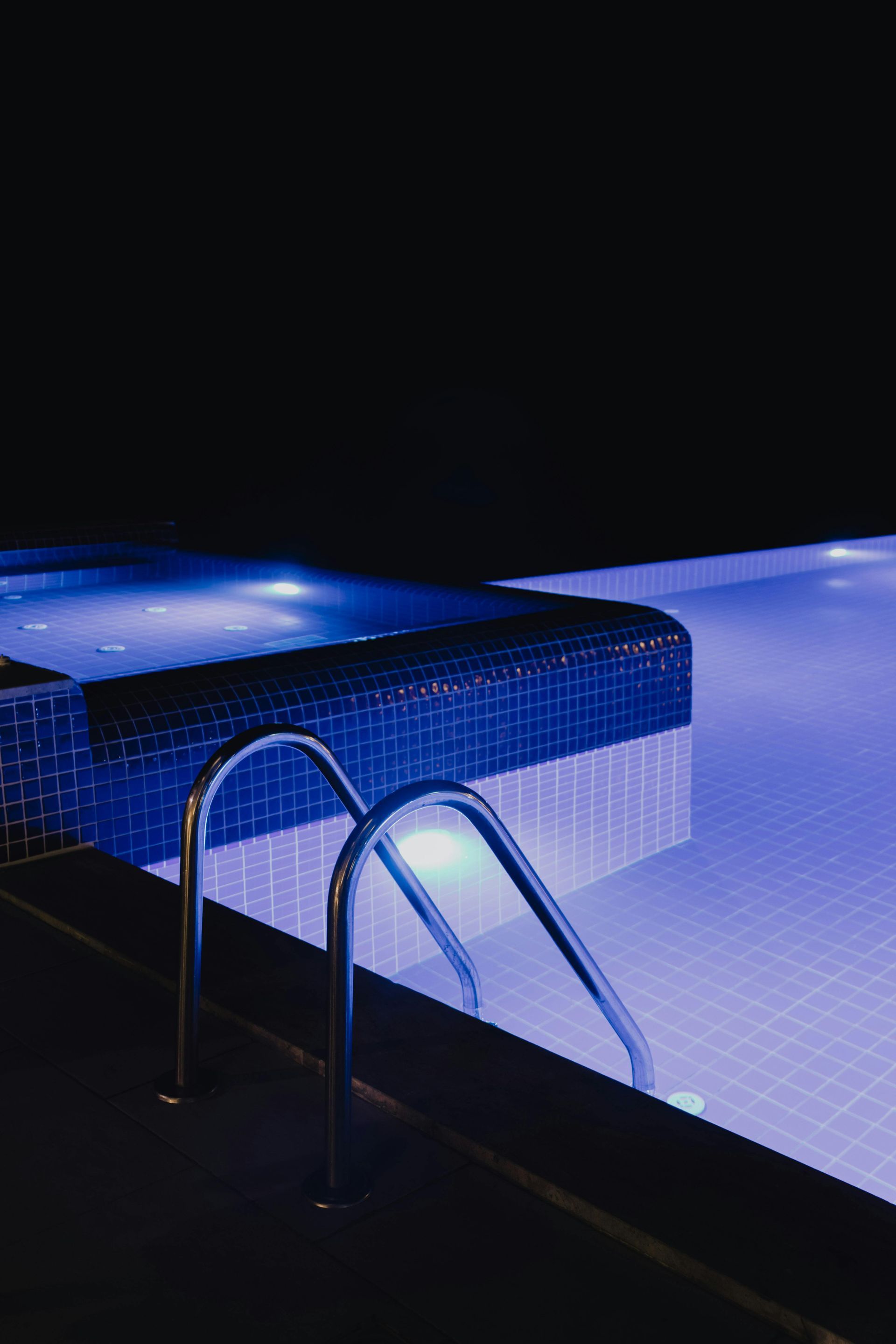Blue-tiled pool with metal ladder and glowing water at night