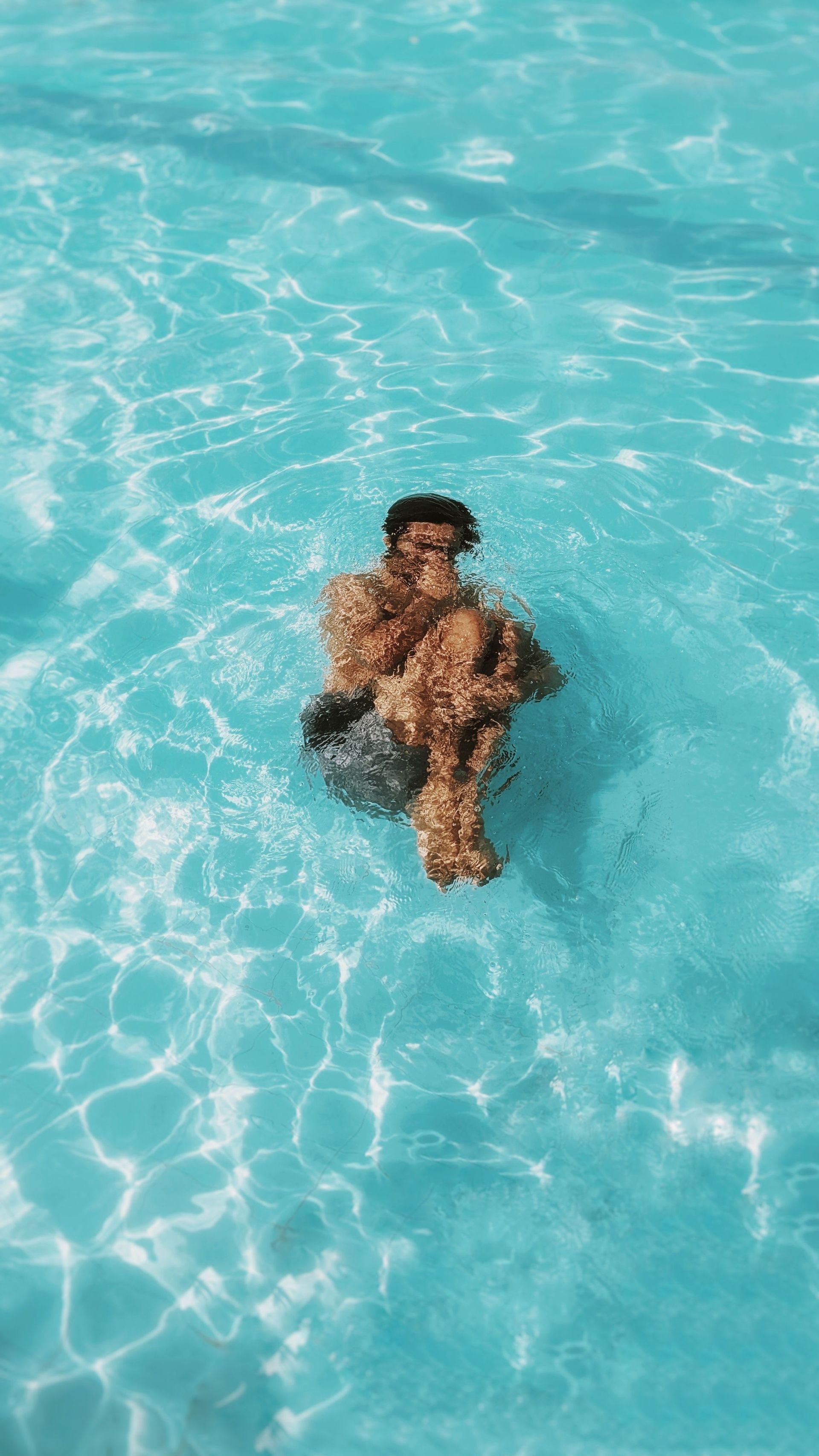 Person swimming in bright blue water, seen from above.