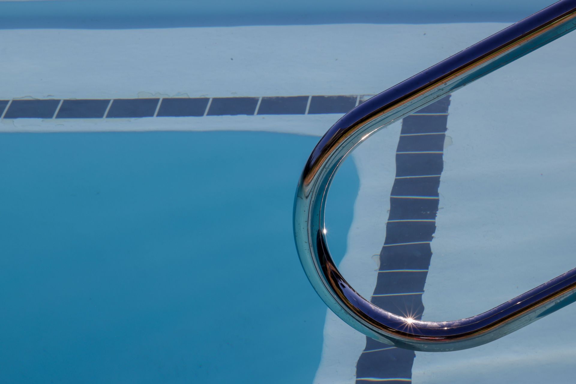 Pool ladder rail over blue swimming pool water and tiled edge