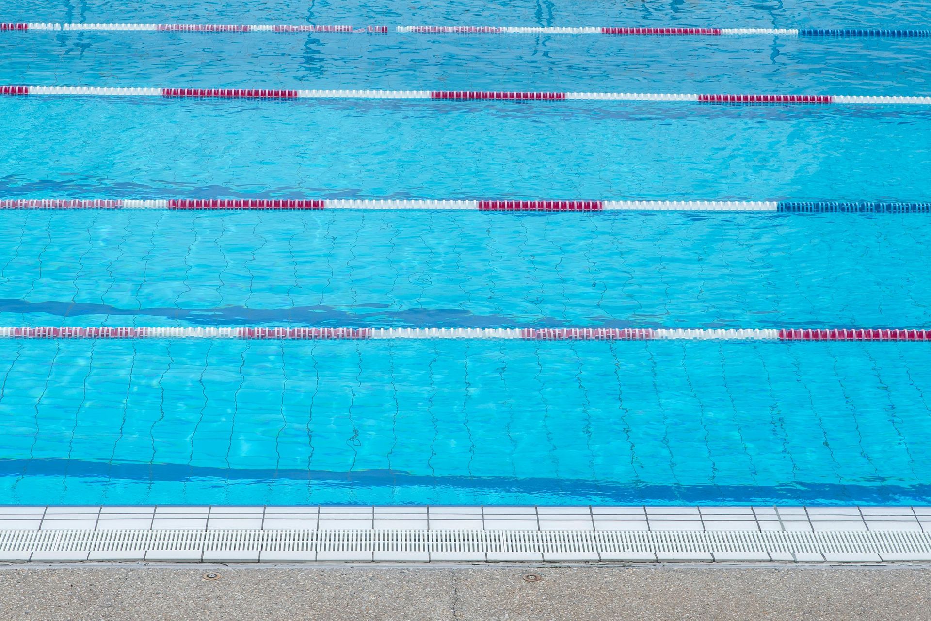Empty outdoor swimming pool with bright blue water and lane ropes, viewed from above