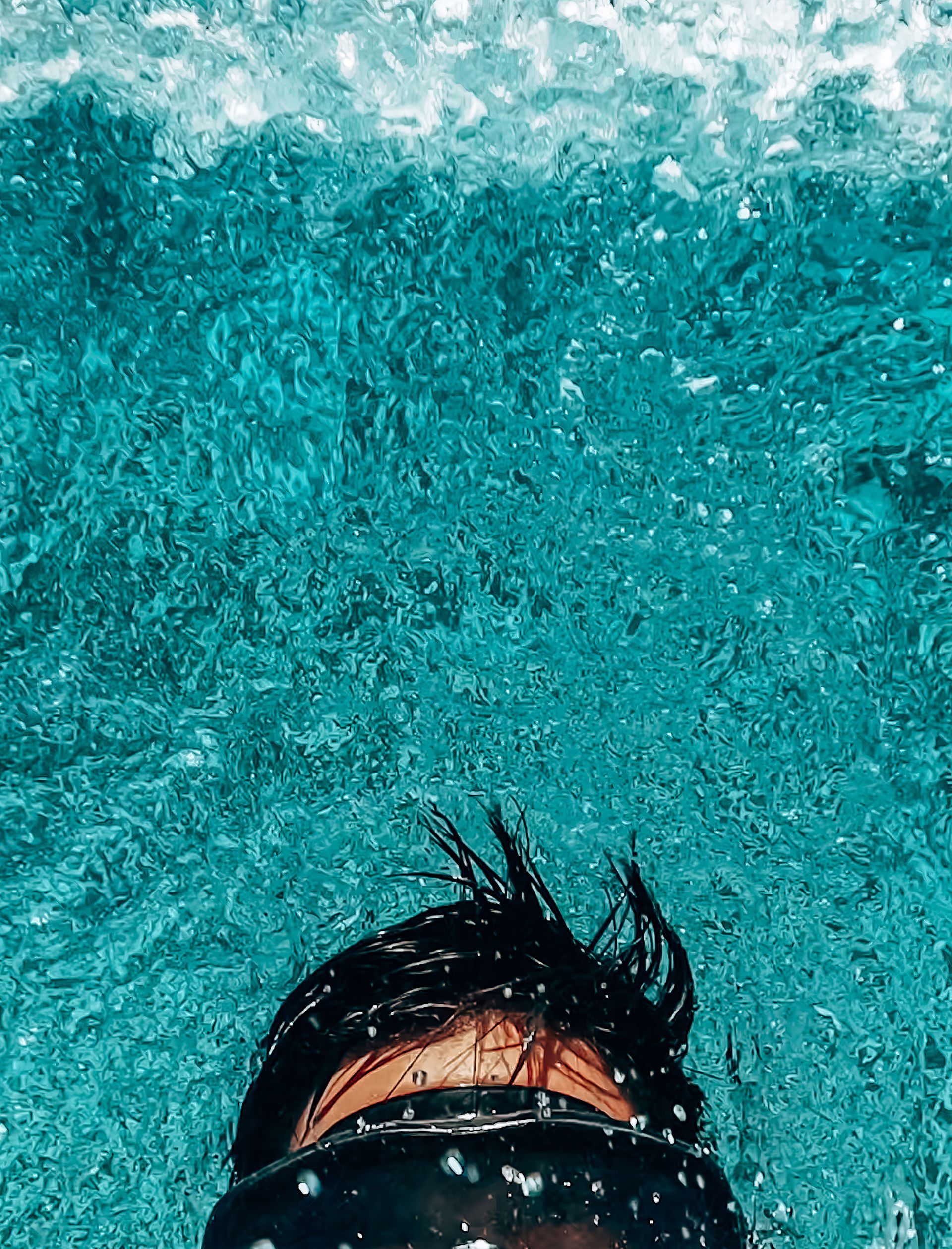 Person swimming in bright turquoise water, with only the top of the head visible near the surface