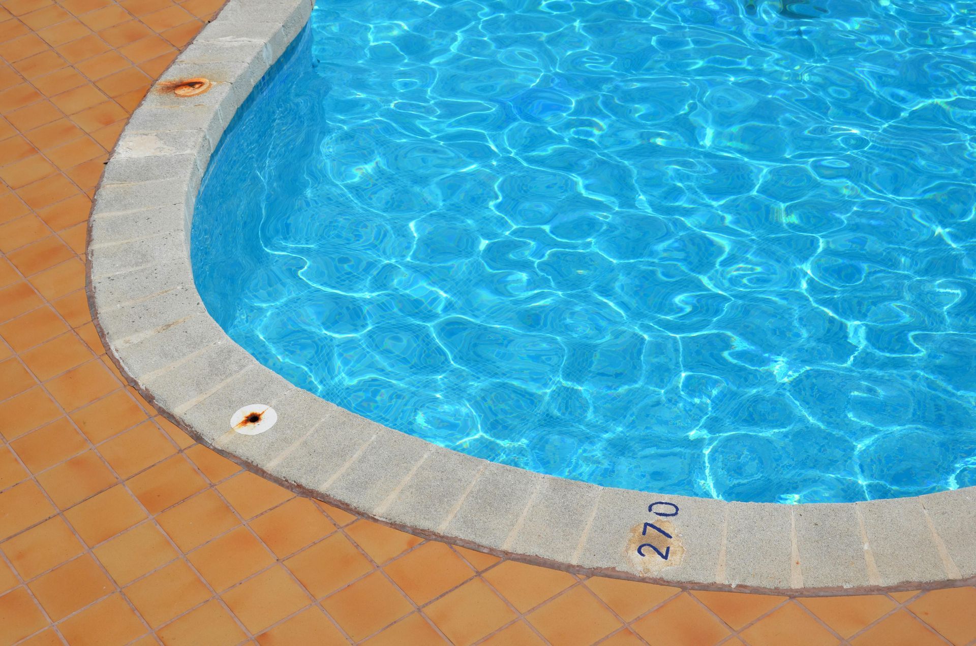 Curved swimming pool edge with blue water and tan tiled deck