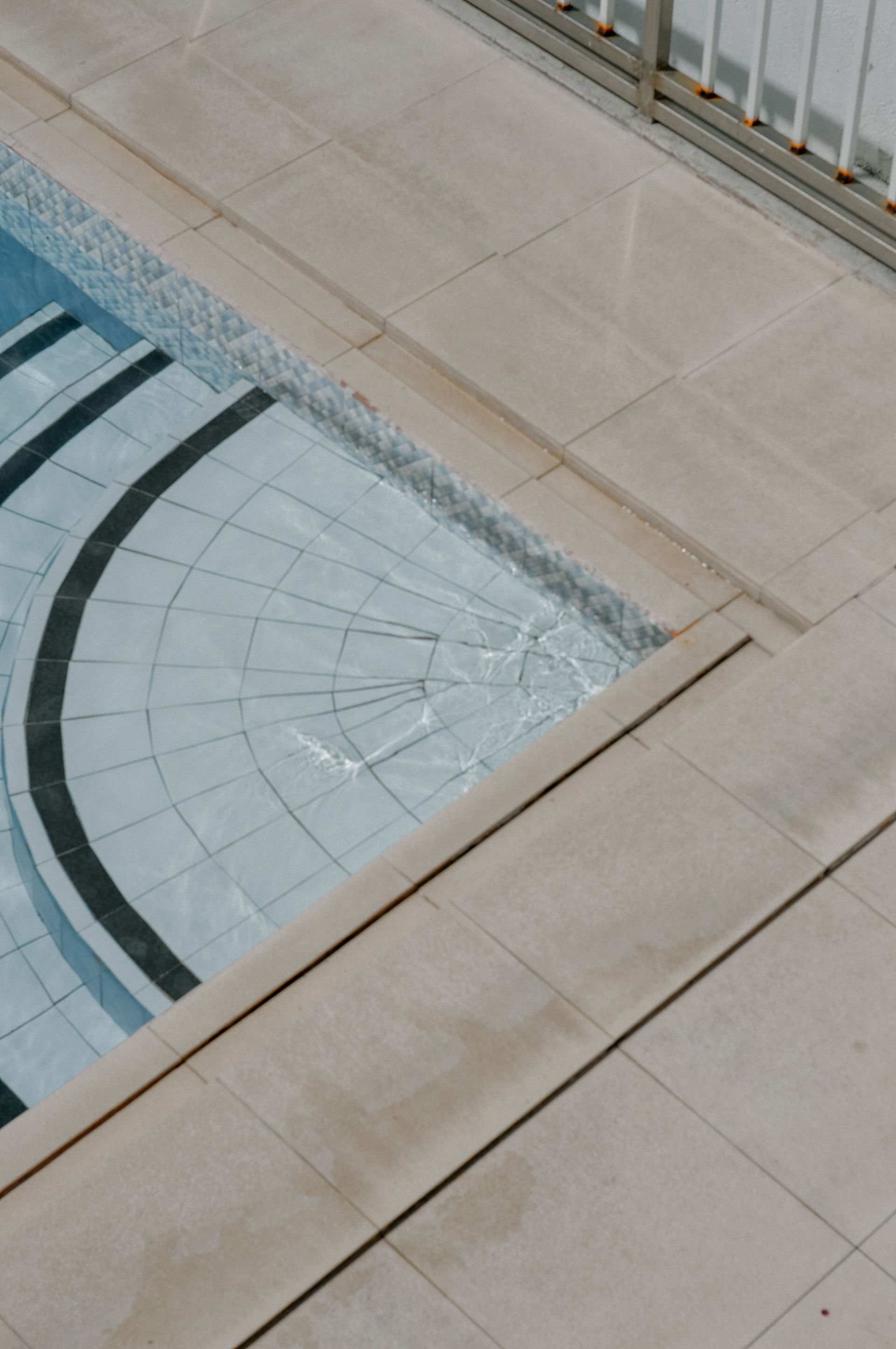 Glass pool corner beside beige stone walkway and metal railing