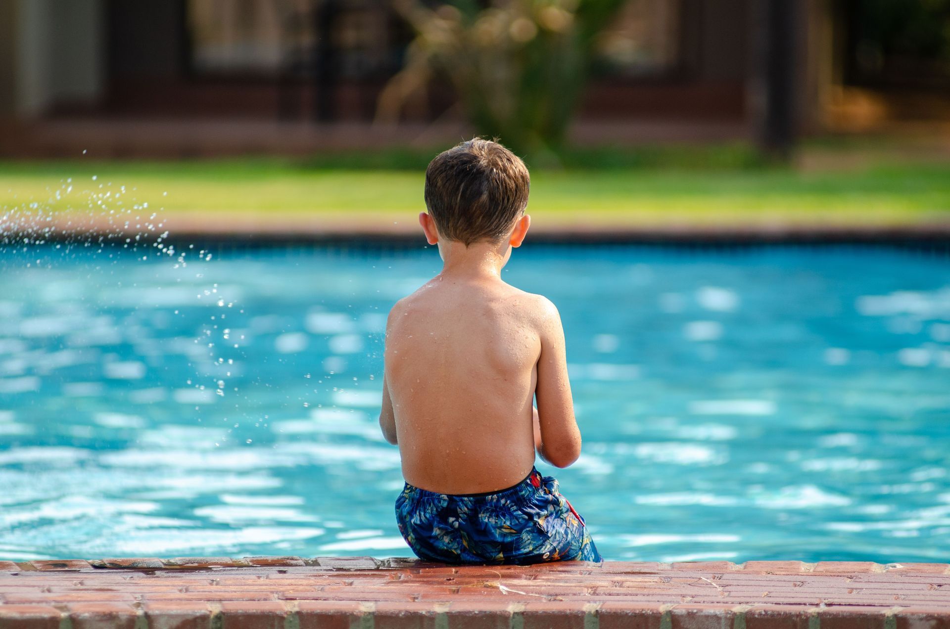 Child sitting by a swimming pool with water splashing nearby