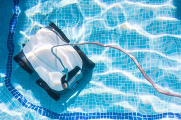 Pool vacuum cleaner floating in blue tiled water, with a hose attached