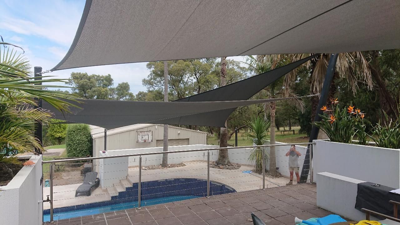 Shade sail installation in Upper Beaconsfield VIC 3808 — featuring multiple overlapping triangular canopies providing sun protection over a residential pool and outdoor entertaining area, bordered by glass fencing, tropical landscaping, and garden structures in a private, tree-lined setting
