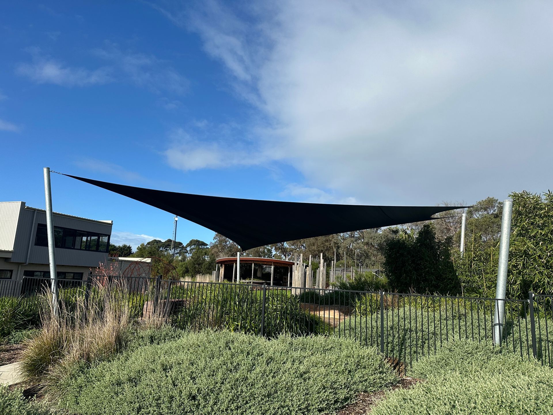 Custom Hyperbolic shade sail installation at Our Lady Star of the Sea Primary School in Cowes, covering outdoor amphitheatre and adjacent playground area with UV-resistant fabric tensioned on tall steel posts, providing sun protection in a landscaped school setting