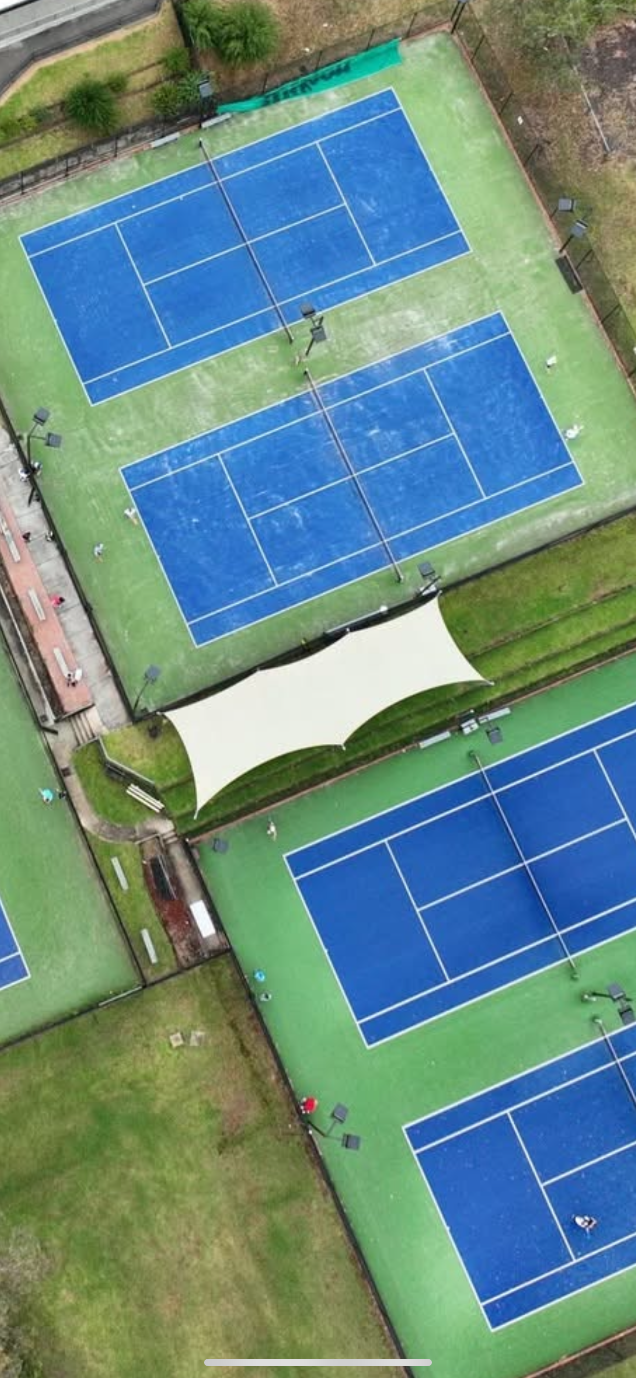 Large commercial-grade shade sail at Endevourhills Tennis Club covering spectator area in front of tennis court, offering all-weather protection and improving outdoor usability and aesthetics of the venue in a green recreational setting