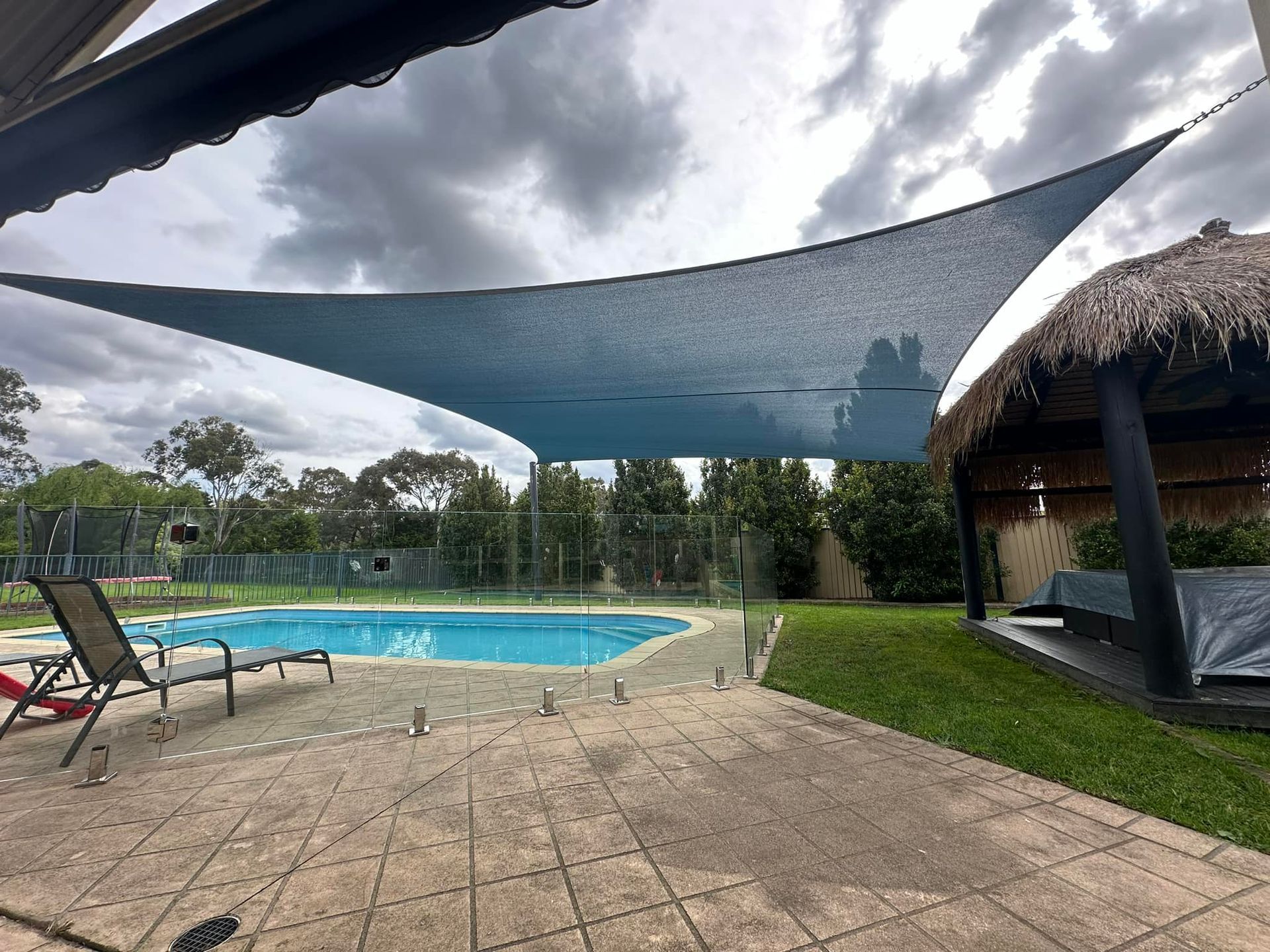 Aqua blue Hyperbolic shade sail installed over residential swimming pool in Narre Warren North, supported by galvanised metal posts and designed to protect against UV rays while enhancing privacy and outdoor comfort in a landscaped backyard setting