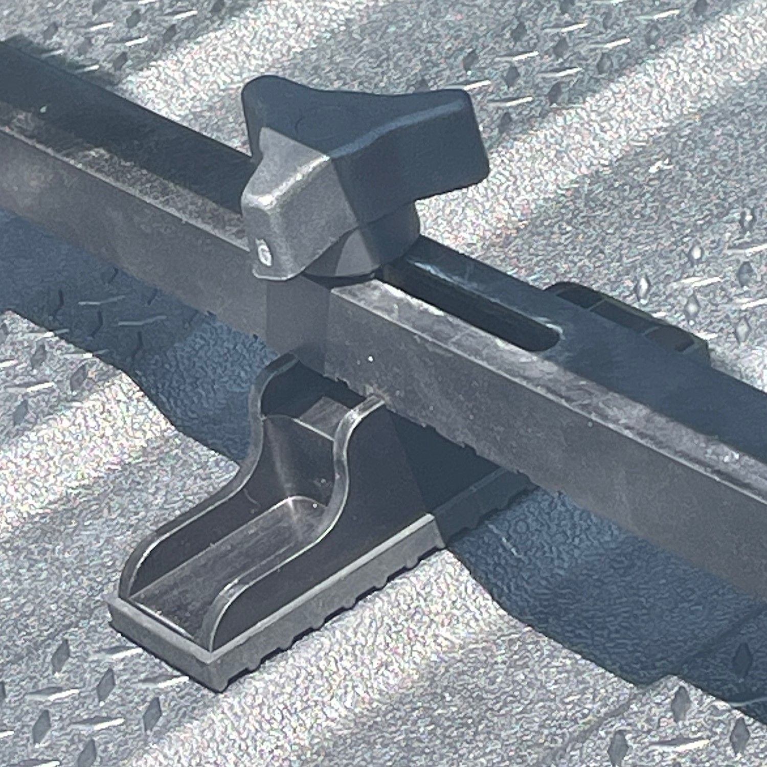 Black adjustable truck bed cargo holder, attached to a textured surface.