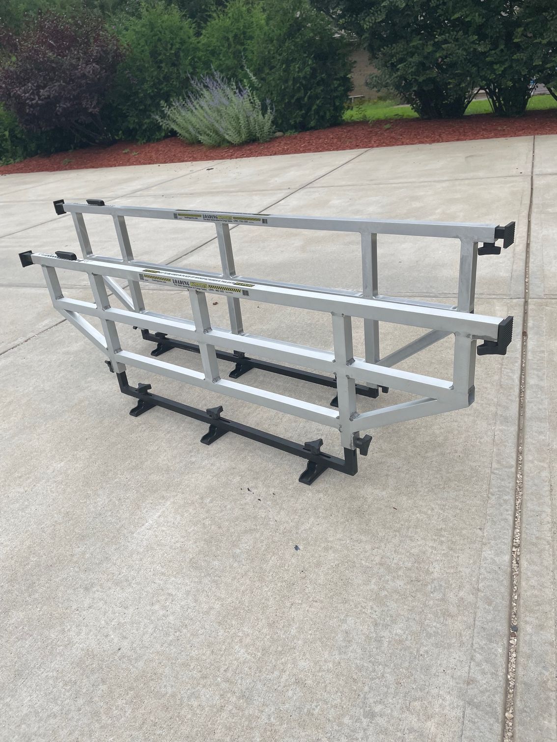 Gray metal frame cargo carrier on a concrete driveway with a garden in the background.