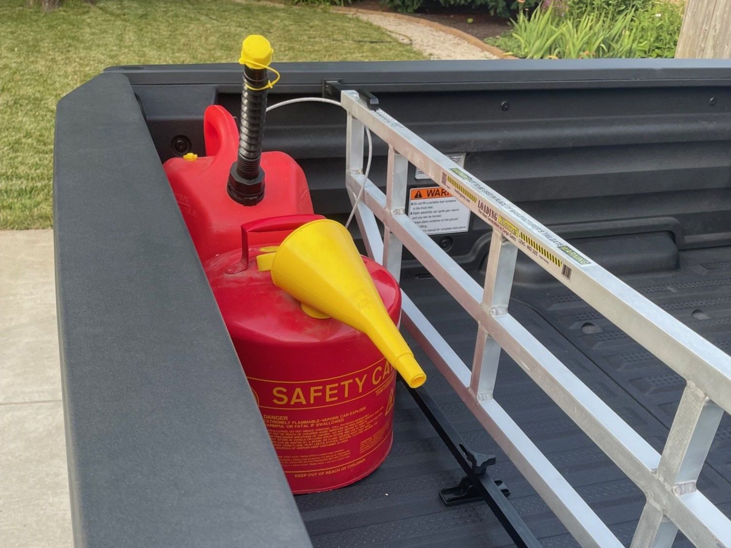 Red gas can and yellow funnel in the bed of a pickup truck, next to a metal bed divider.