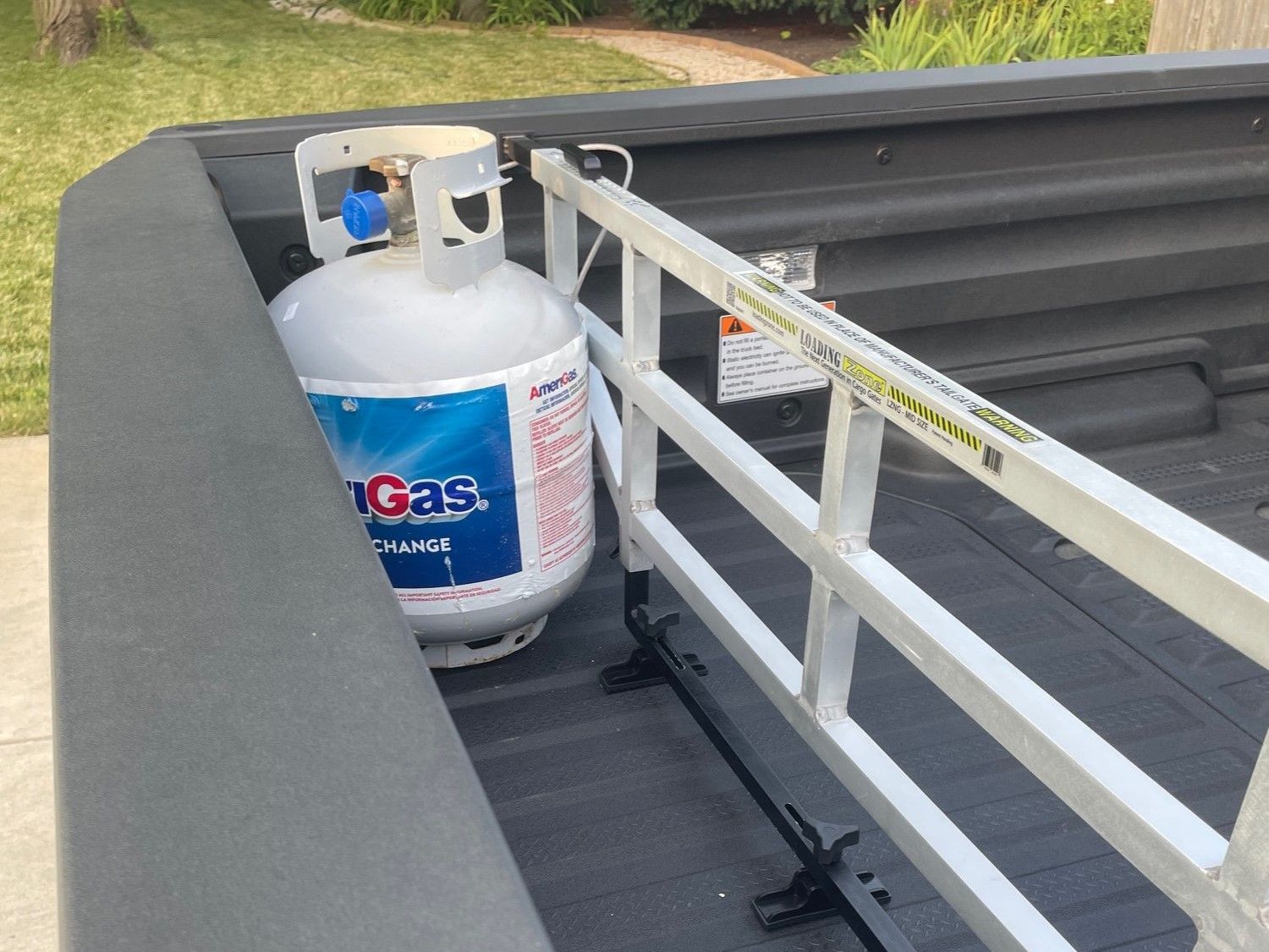 Propane tank secured in a black truck bed behind a white cargo divider.