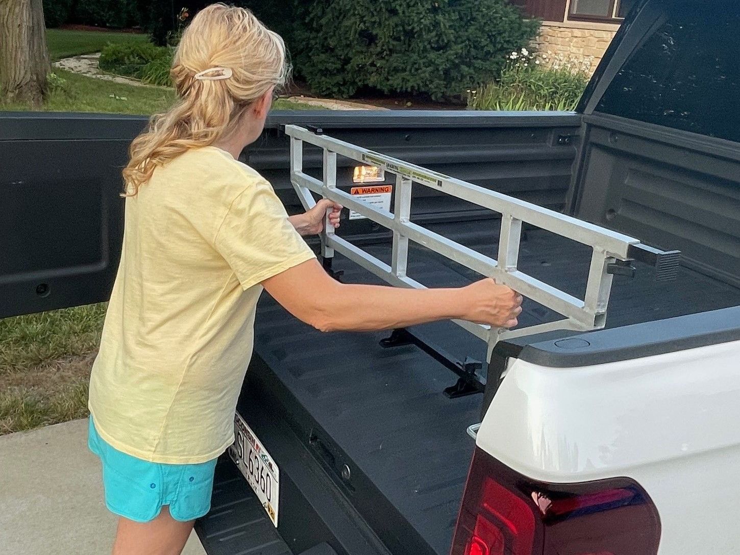 Woman placing a cargo bed extender into a white pickup truck.
