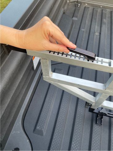 Hand placing a black object on a metal truck bed rack, set inside a gray truck bed.