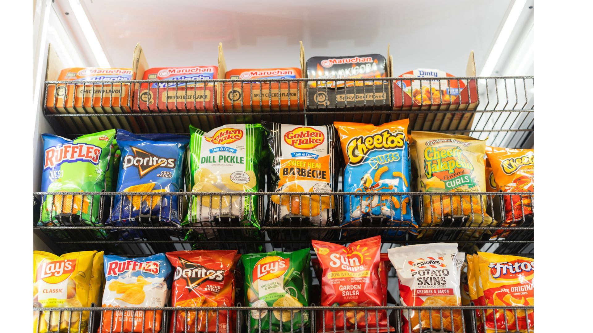 A retail display with three vertical sections filled with various snack bags, candy, and a self-checkout terminal.