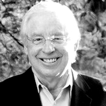 A man wearing glasses and a suit is smiling in a black and white photo.
