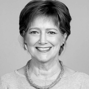 A black and white photo of a woman wearing a necklace and smiling.