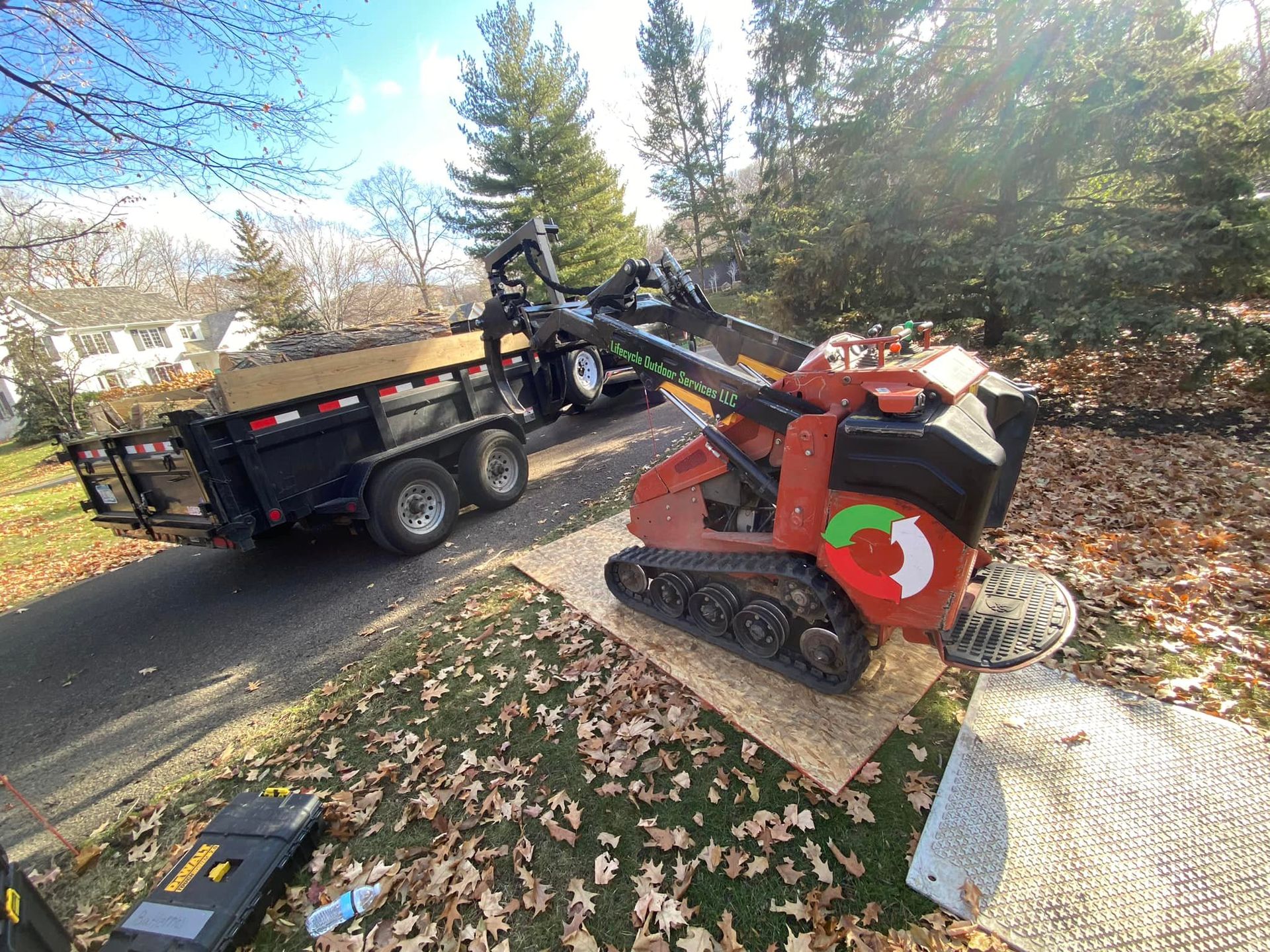 Red and black tracked machine and trailer on a driveway.