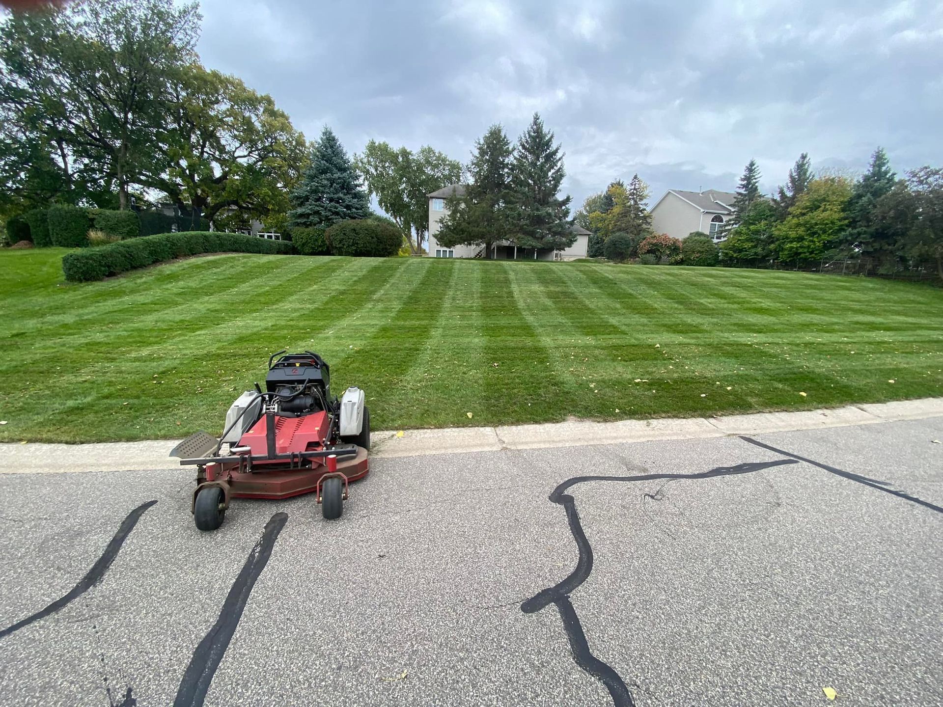 Lawnmower on pavement next to a freshly mowed lawn with stripe pattern, under cloudy sky.