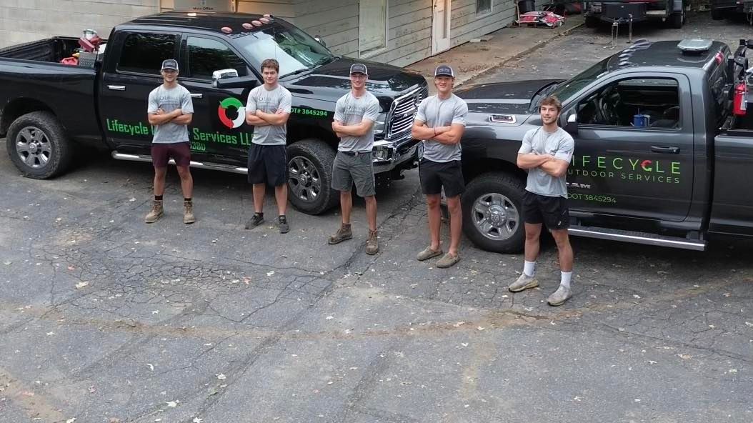 Five men in front of two black trucks with logo; men are in work uniforms with arms crossed.