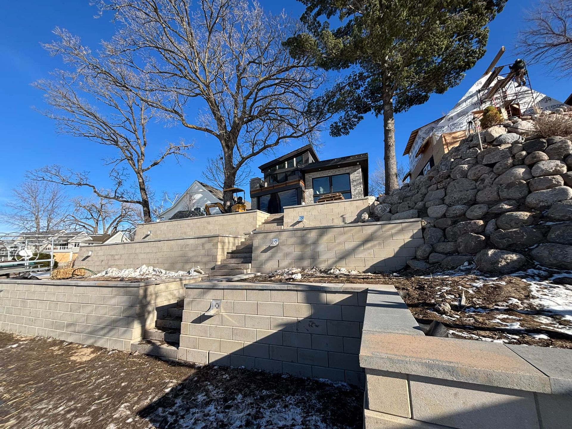 Construction site with retaining walls, steps, and a partially built home under a clear sky.