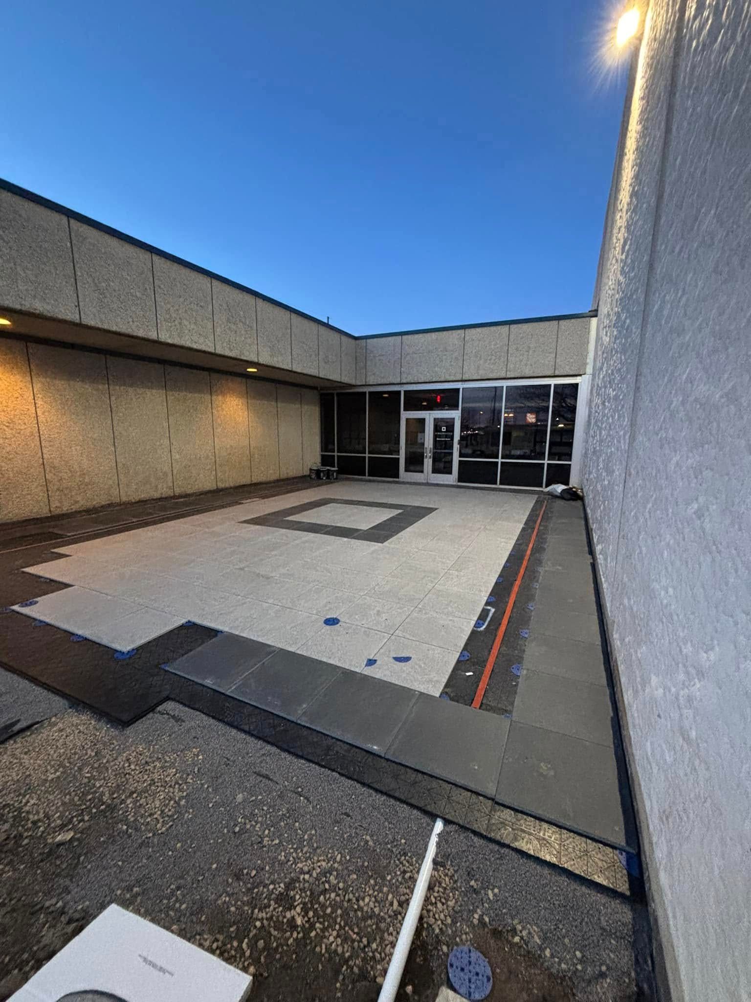 Exterior view of a commercial building entrance with partially installed dark gray tiles and a clear blue sky.