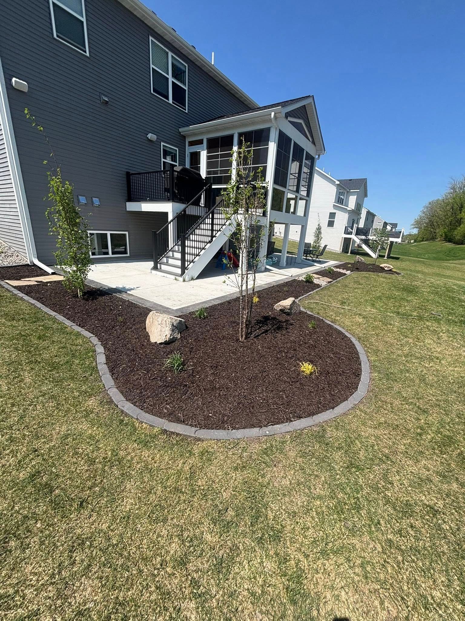 Backyard landscaping with a screened-in porch, patio, mulched flowerbed, and grass lawn.