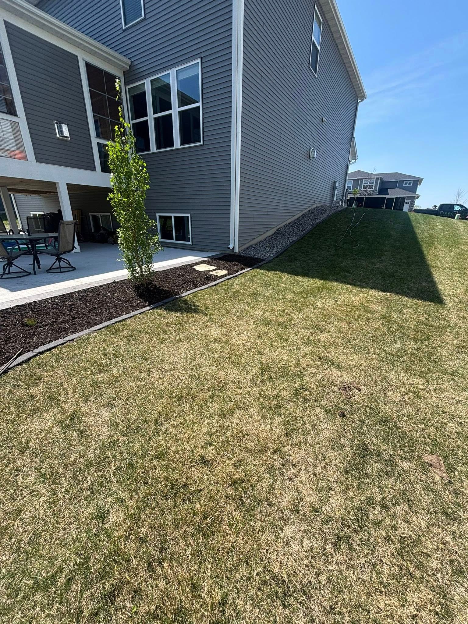 Exterior view of a house with gray siding, a patio, and a grassy lawn in sunlight.