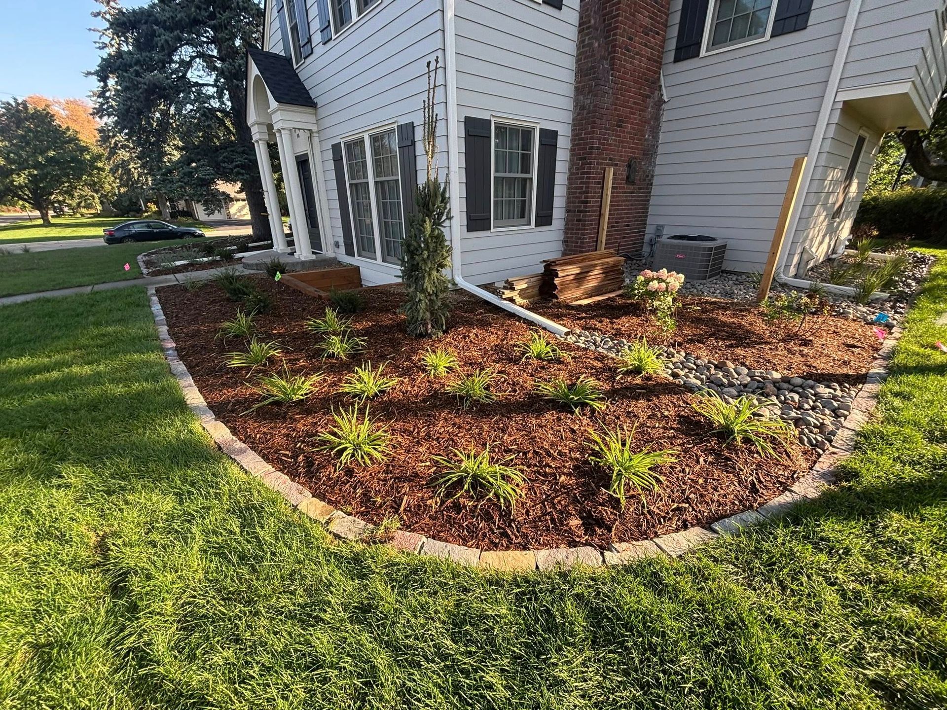 A house with a newly mulched flower bed edged with stone.