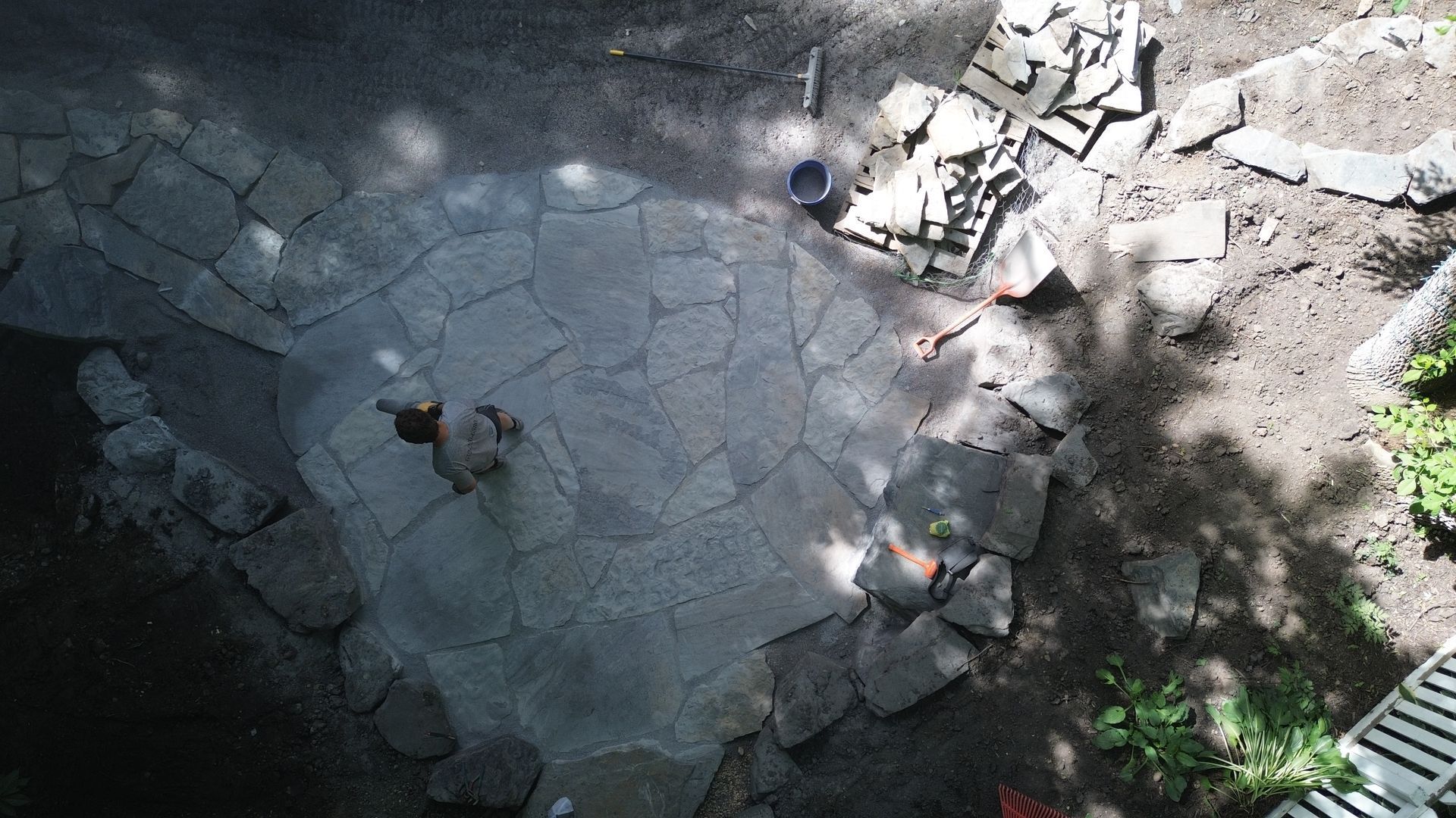 Stone patio under construction with scattered stones and a person working.